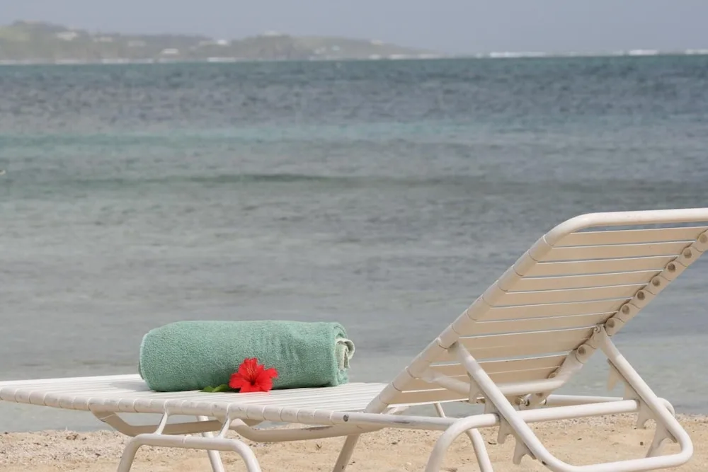 Beach lounge chair with a rolled towel and red flower by the water at Hotel on the Cay.