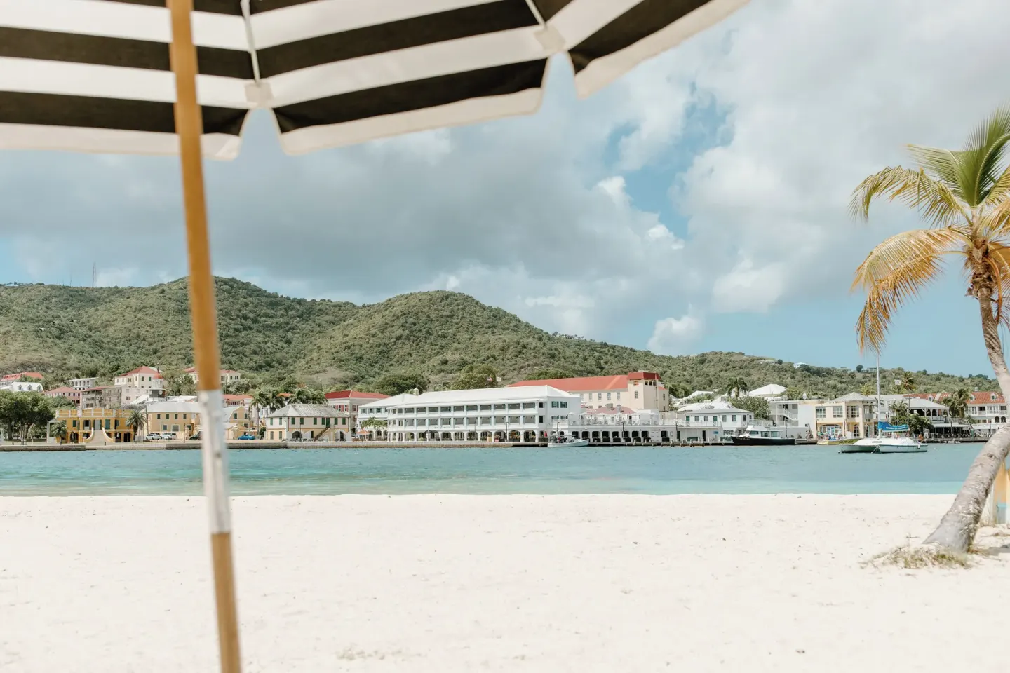 Beach umbrella, palm tree and harbor-facing buildings across the water at Hotel on the Cay.