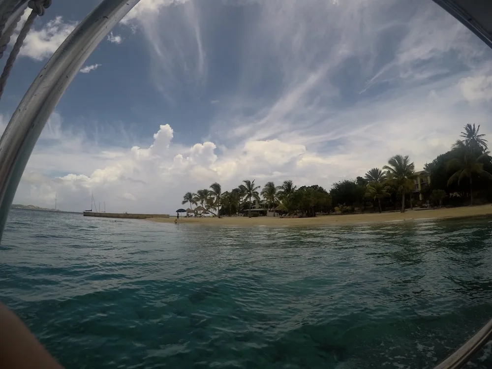 Hotel on the Cay beachfront is seen from the water with palms and clouds overhead.