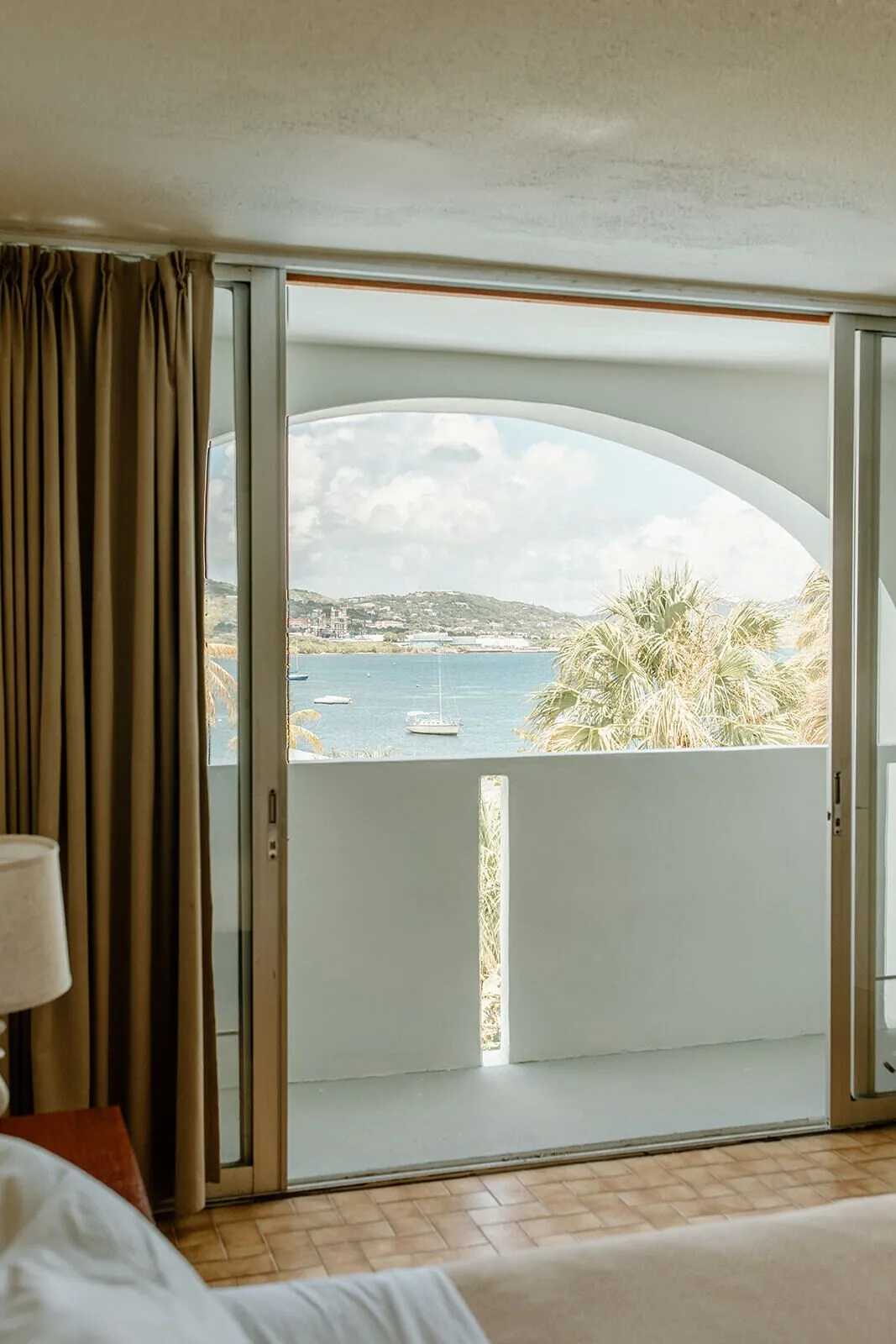 Sliding doors open to a balcony with water, boats, palms, and hills at Hotel on the Cay.
