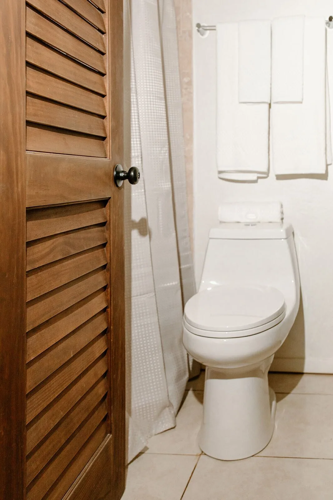 Bathroom toilet beside a shower curtain and wooden louvered door at Hotel on the Cay.