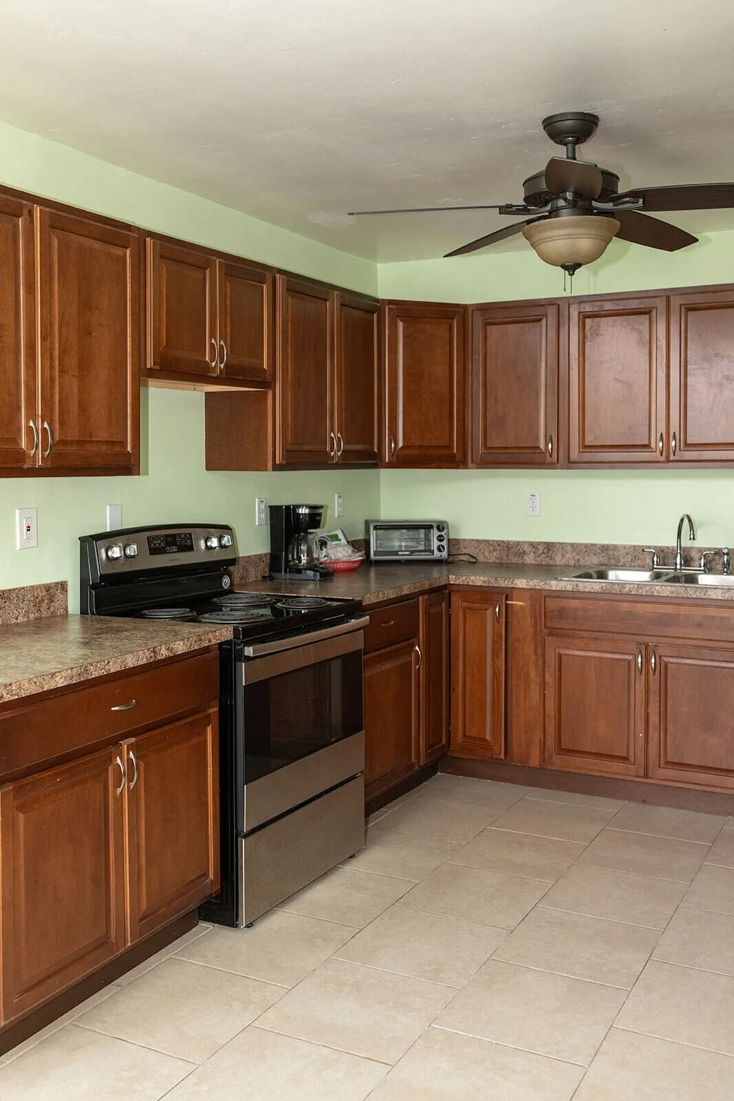 Guest room kitchen with wood cabinets, stove, coffee maker, sink, and ceiling fan at Hotel on the Cay.