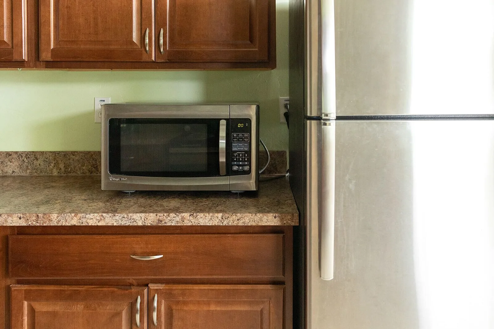 Guest room kitchen with wood cabinets, microwave, granite-look counter, and refrigerator at Hotel on the Cay.