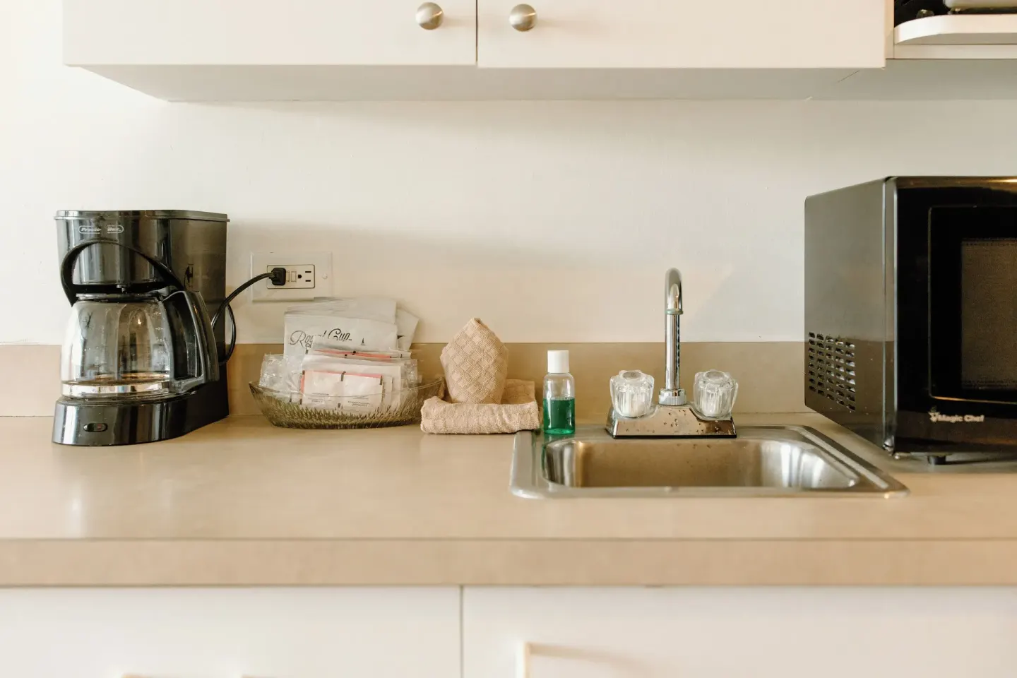 Guest room kitchenette counter with coffee maker, sink, microwave, cups, and towels at Hotel on the Cay.
