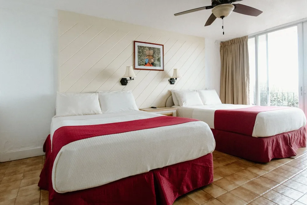 Guest room with two beds, balcony doors, and red bedding accents at Hotel on the Cay.