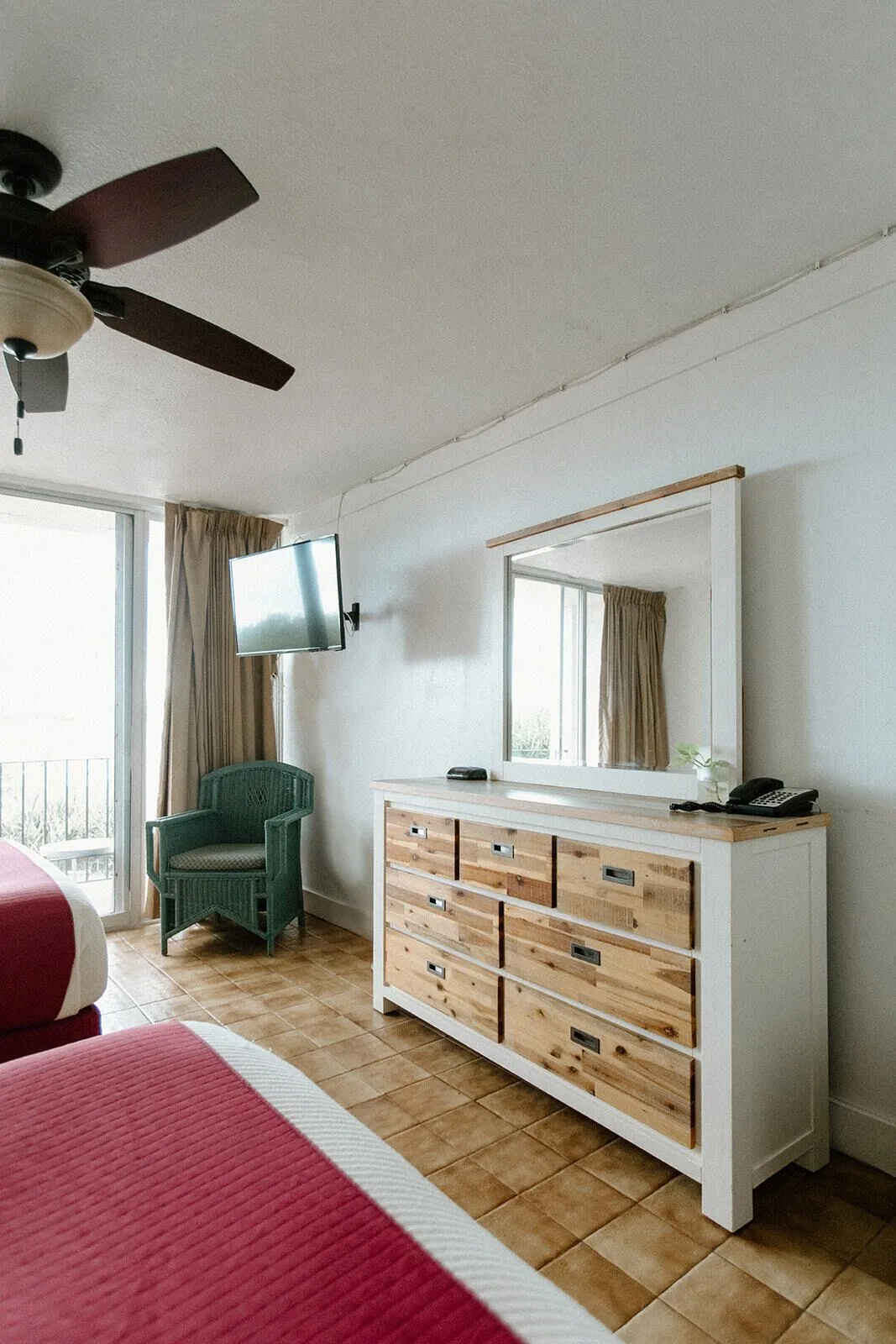 Guest room with two beds, dresser, mirror, TV, wicker chair, and balcony doors at Hotel on the Cay.