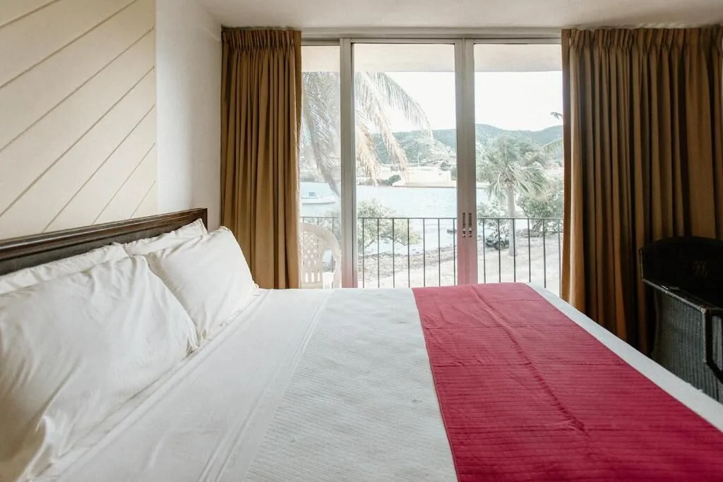 Guest room bed with red runner and sliding doors overlooking water and palms at Hotel on the Cay.