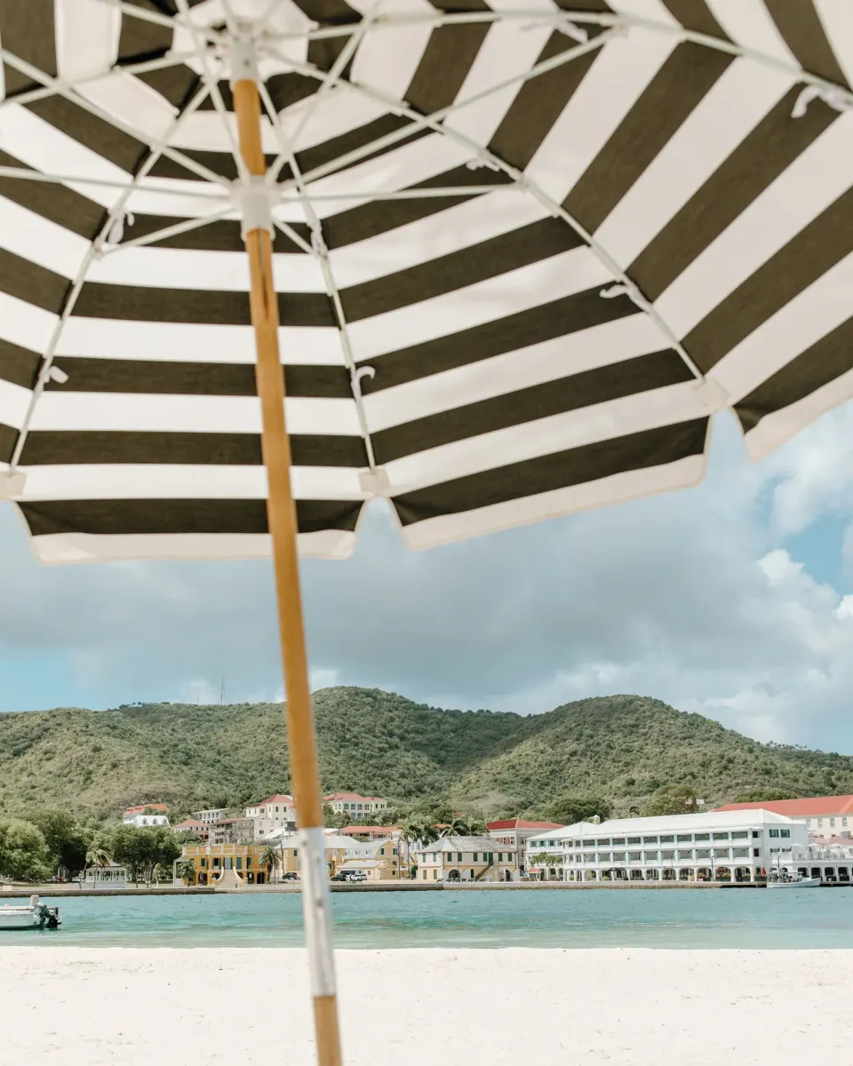 Striped beach umbrella framing harbor, hills and waterfront buildings at Hotel on the Cay.