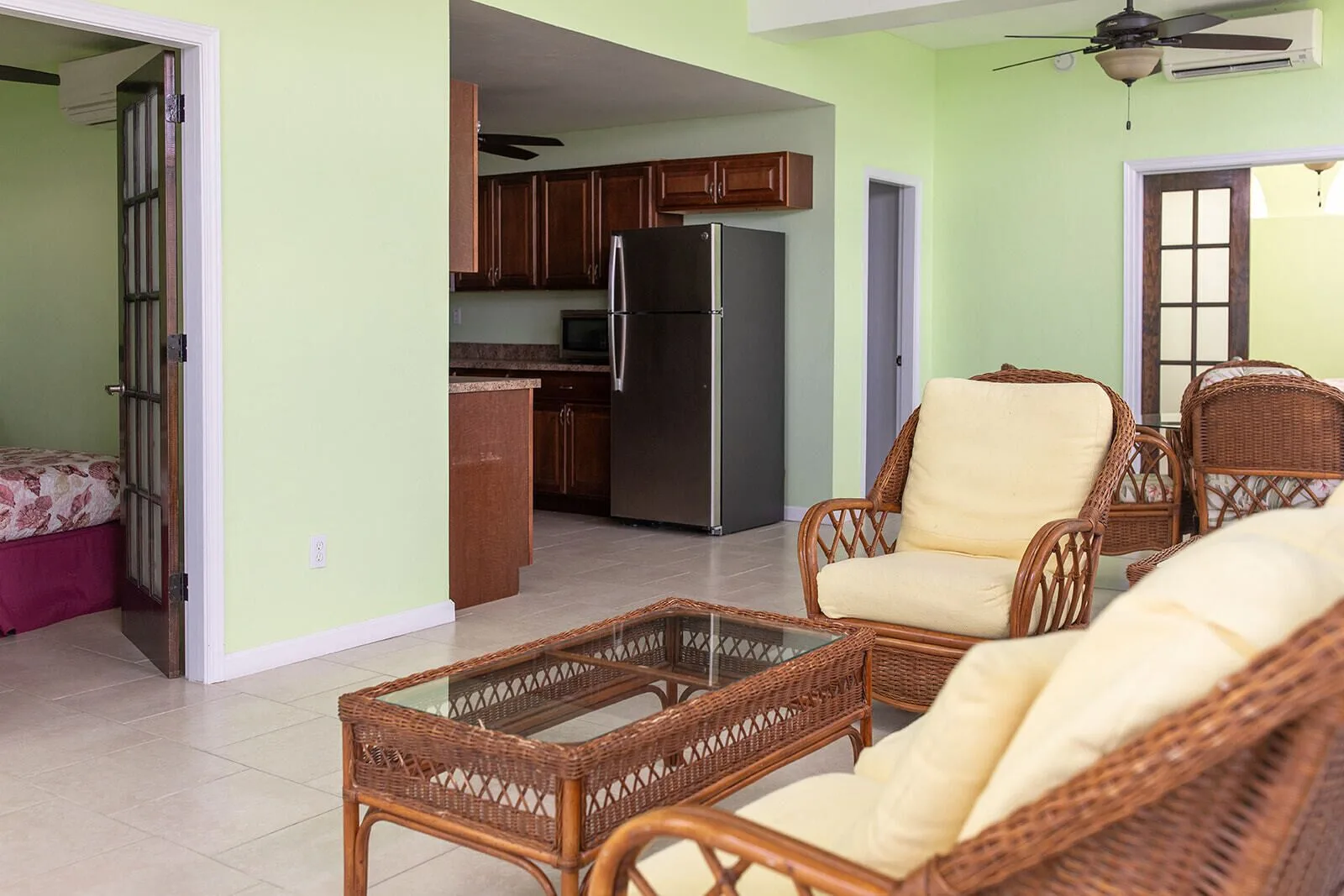 Suite living area with wicker chairs, kitchen, refrigerator, and bedroom doorway at Hotel on the Cay.