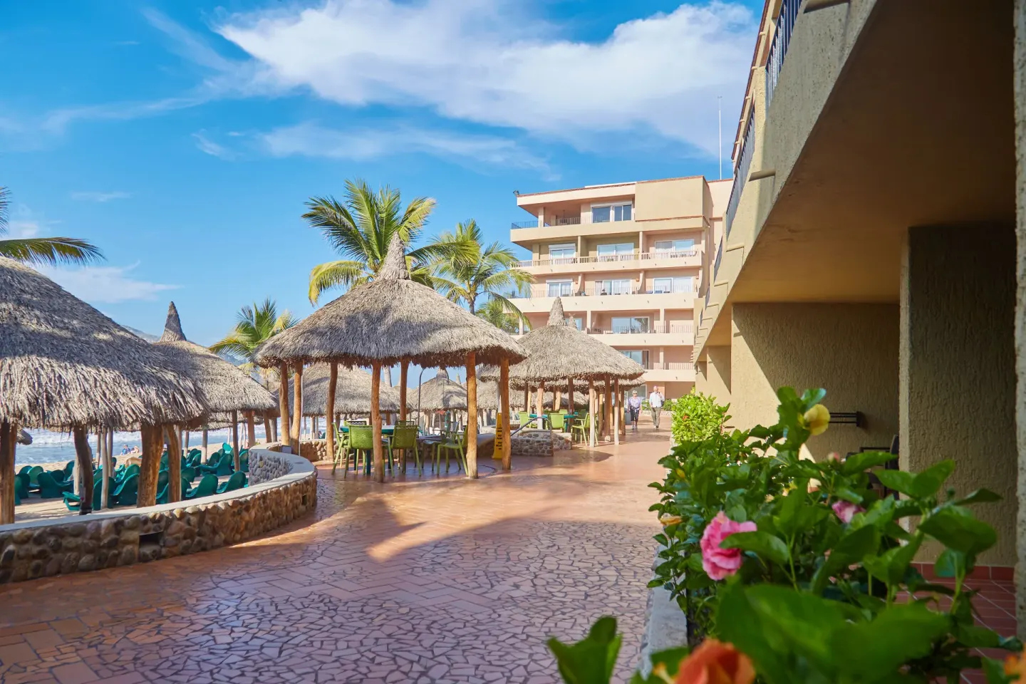Beachfront walkway with thatched palapas and resort buildings at Hotel Playa Mazatlan.