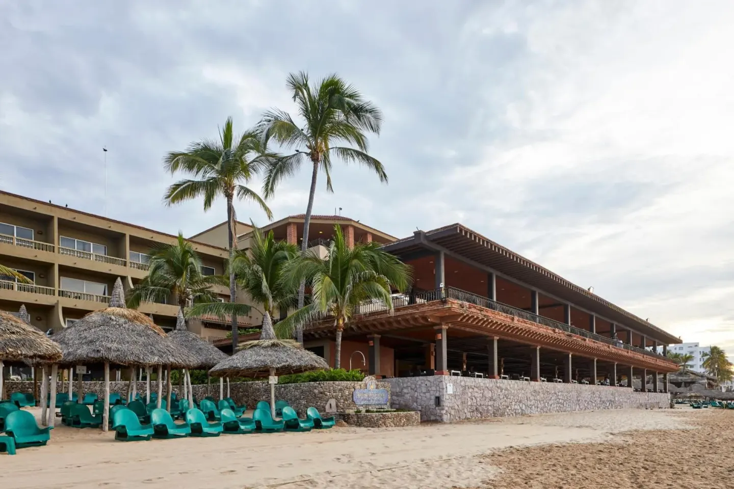 Beachfront resort building with palapas and green loungers at Hotel Playa Mazatlan.