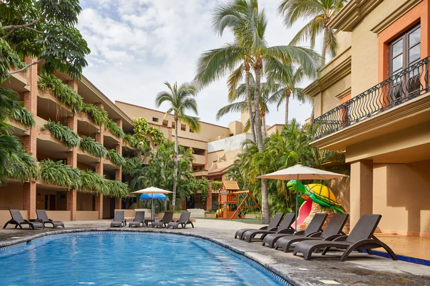 Courtyard pool with loungers, palms, and a children's slide at Hotel Playa Mazatlan.