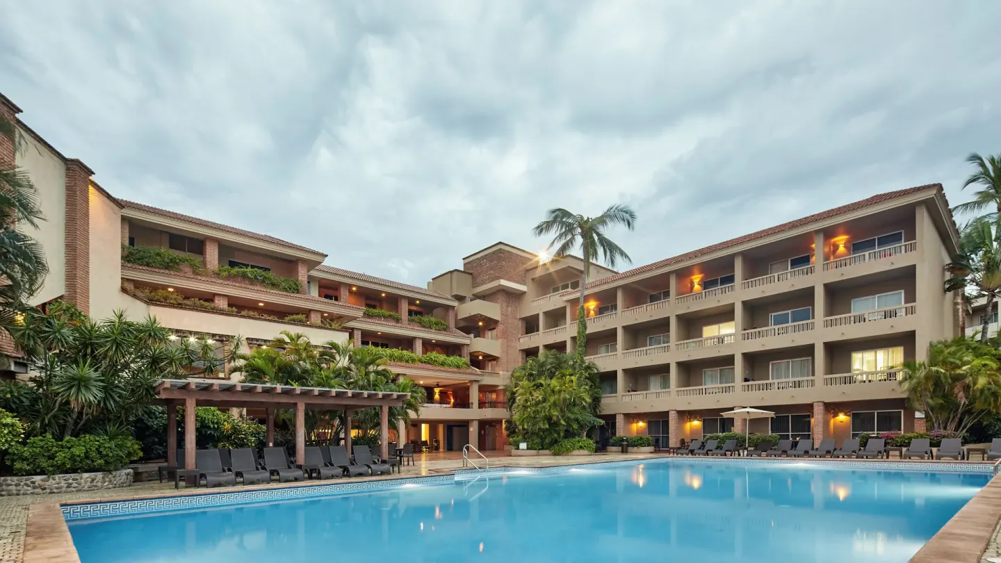 Evening pool courtyard with lit balconies and tropical landscaping at Hotel Playa Mazatlan.