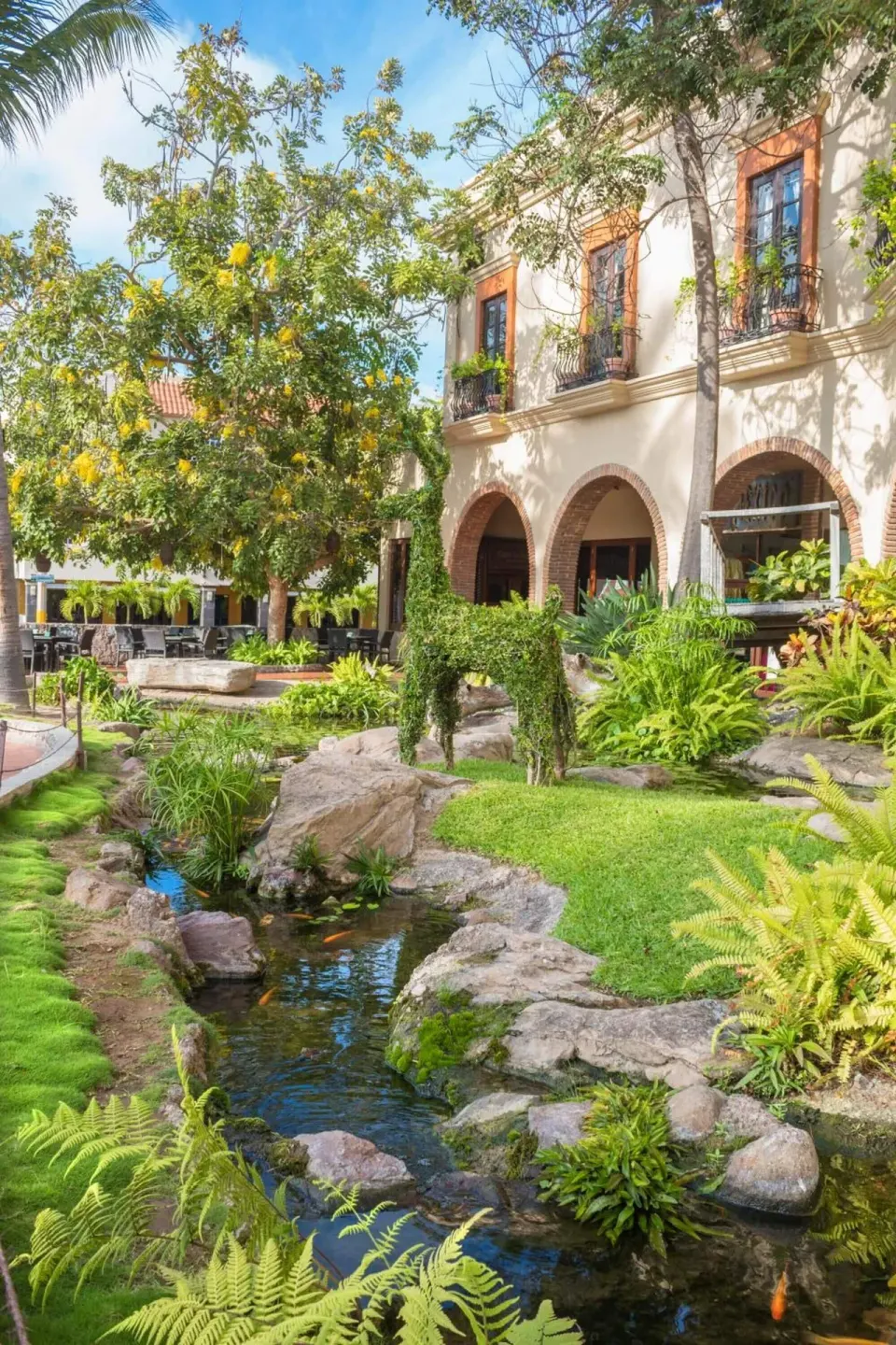 Garden courtyard with stream, rocks, and arched building at Hotel Playa Mazatlan.