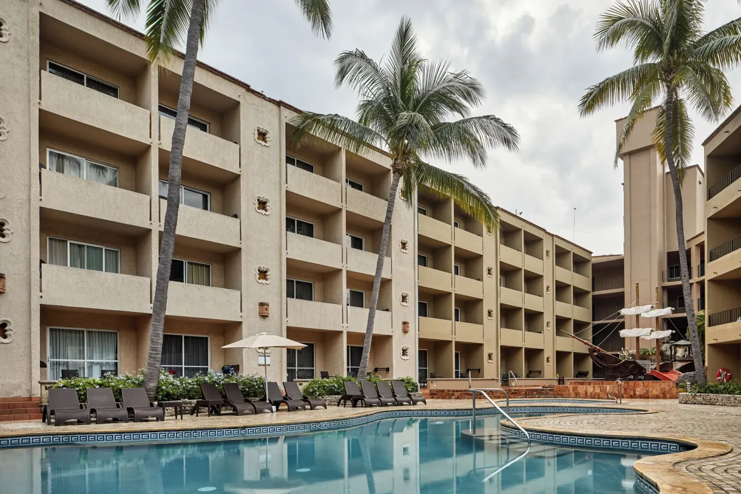 Pool courtyard with lounge chairs, palms and guest balconies at Hotel Playa Mazatlan.