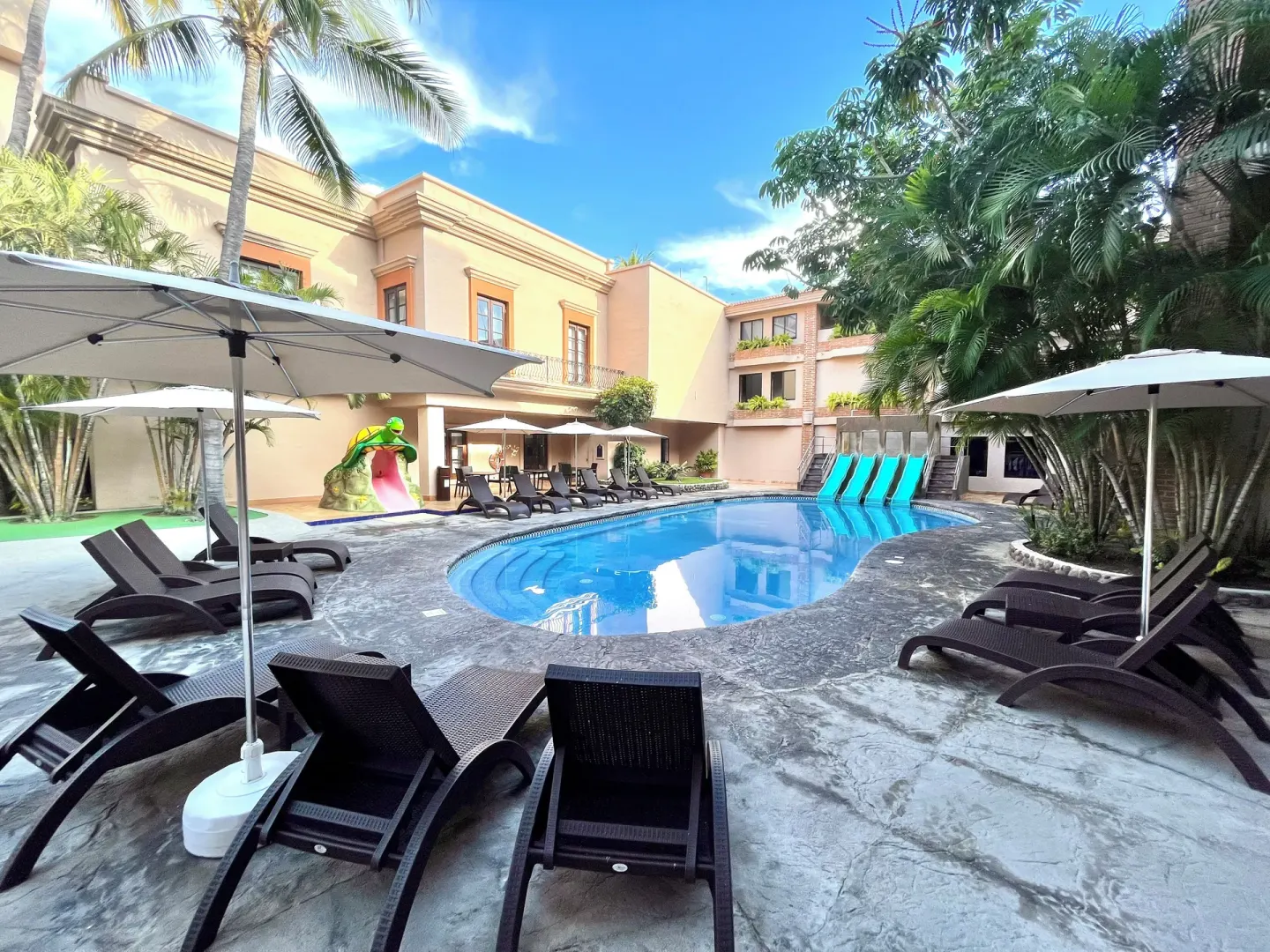 Resort pool with lounge chairs, umbrellas, palms, and a children's slide at Hotel Playa Mazatlan.