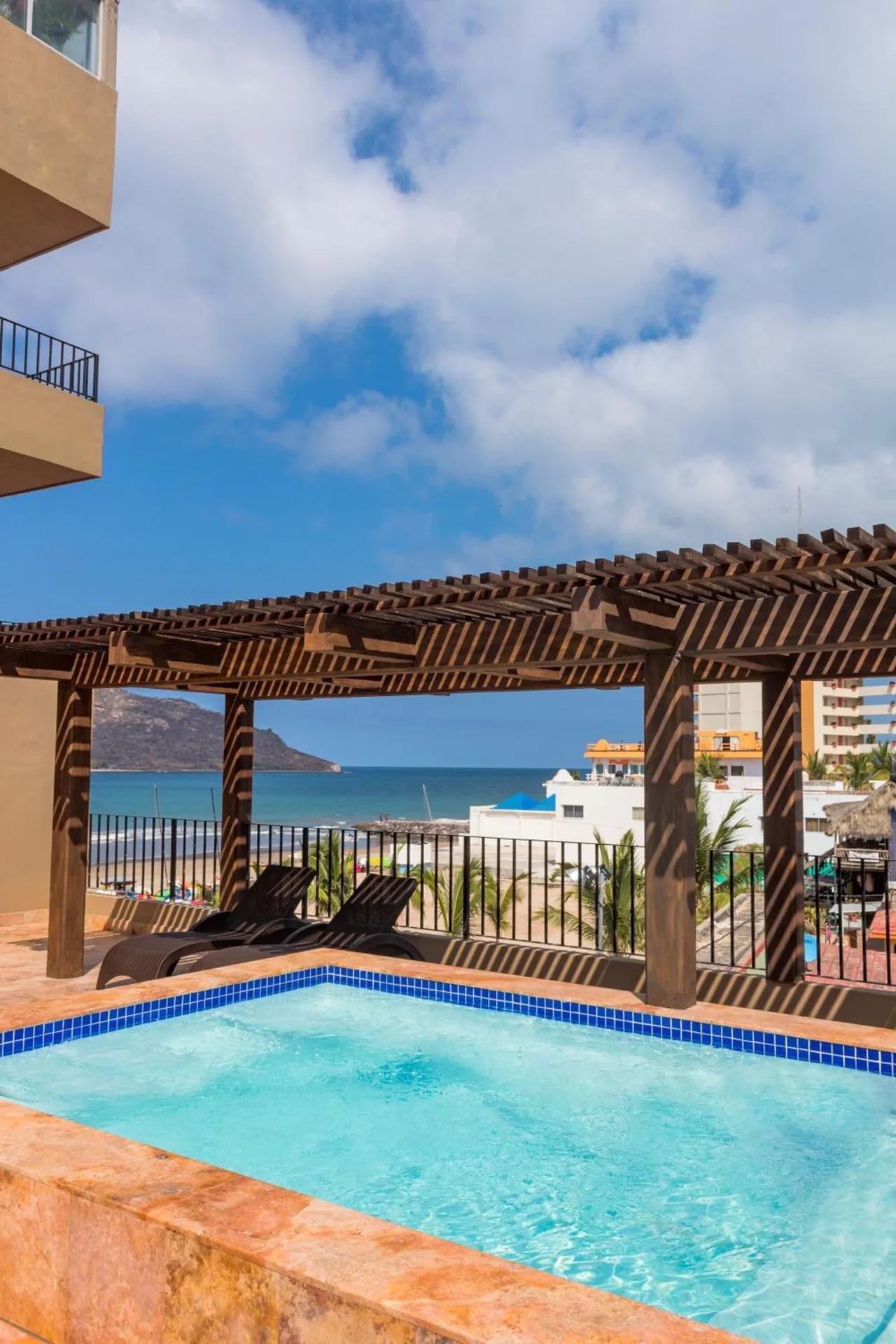 Small pool at Hotel Playa Mazatlan with lounge chairs, pergola, and ocean view.