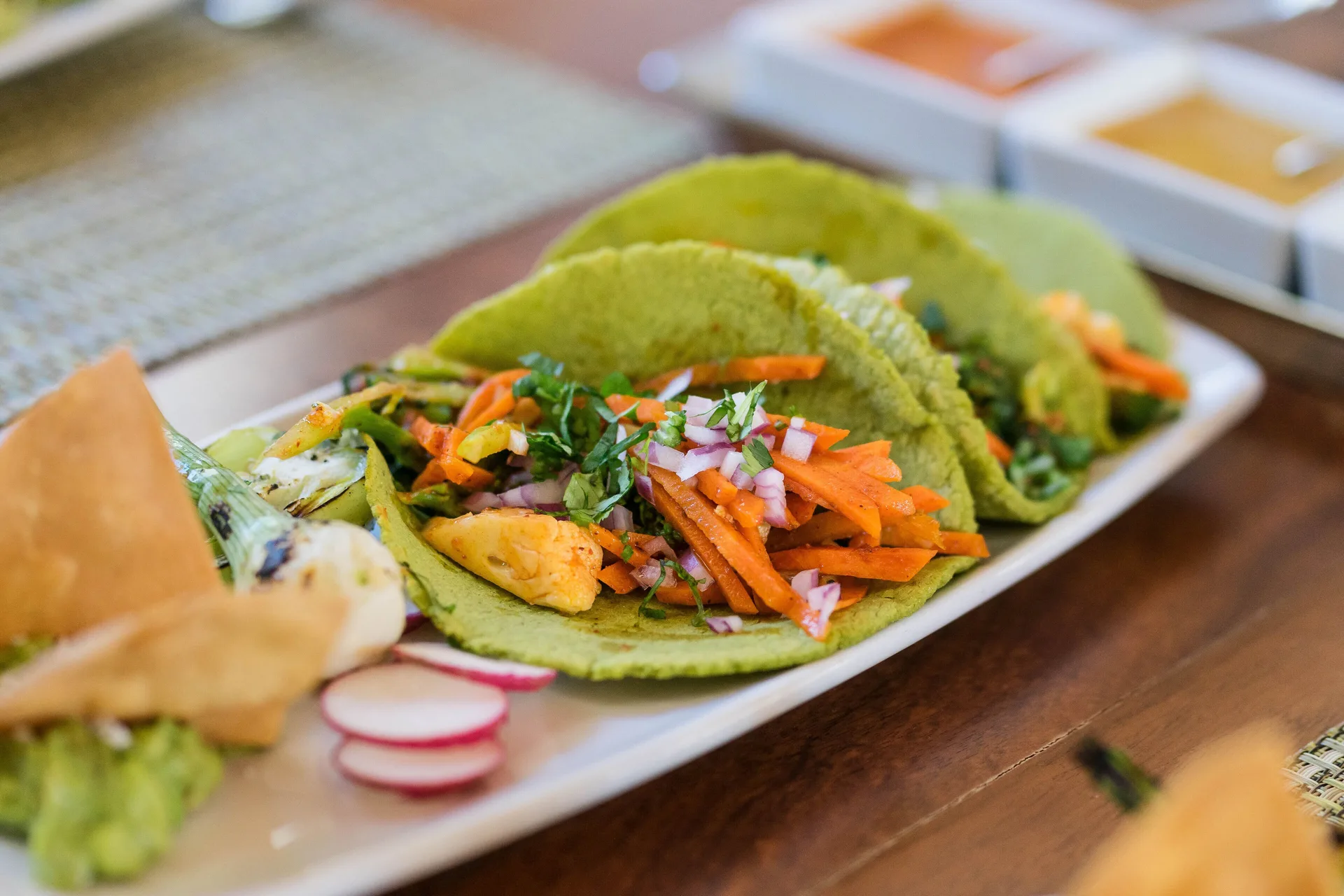 Green tacos with vegetables and sauces on a wooden table at Hotel Playa Mazatlan.