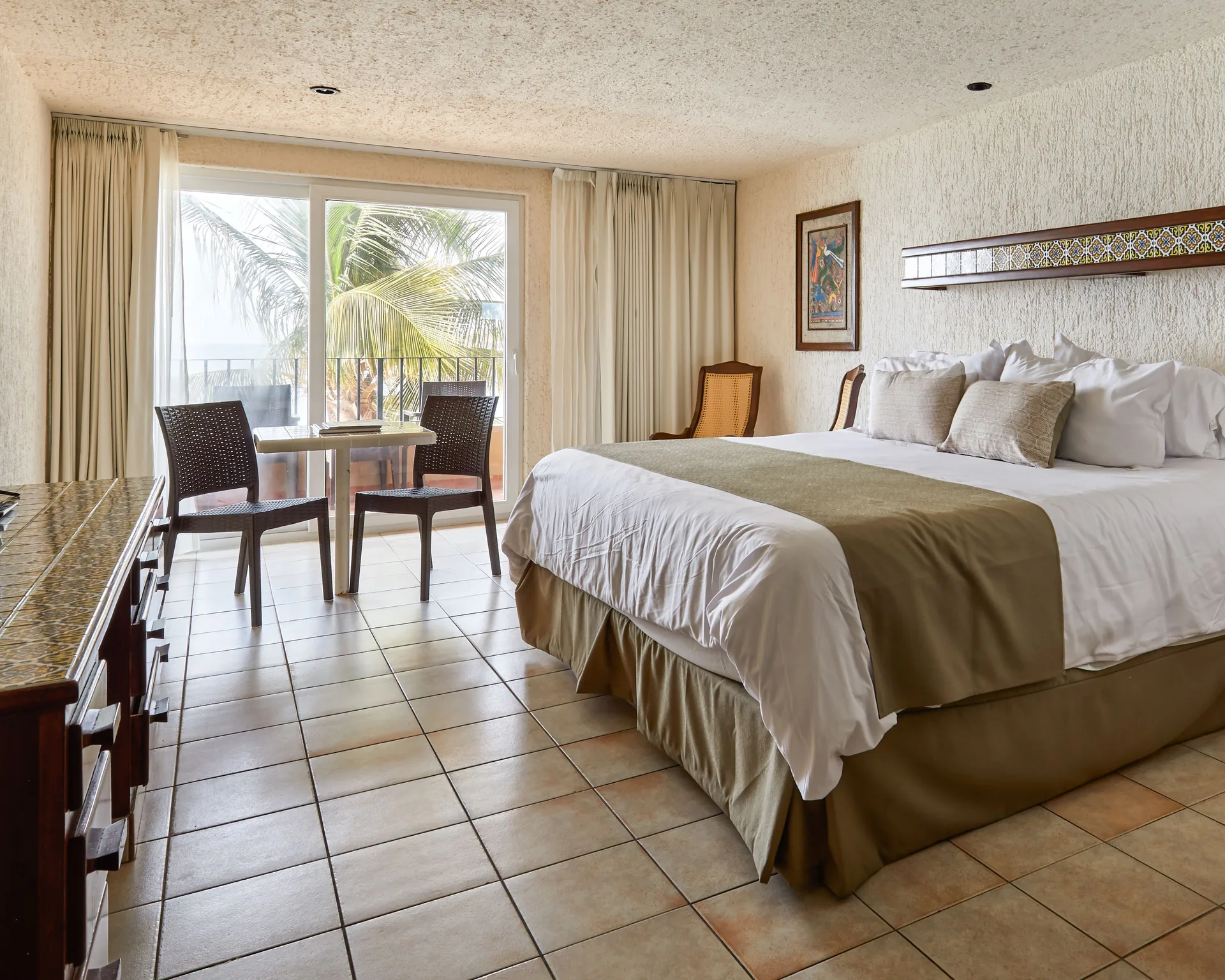 One-bed guest room with balcony seating and palm view at Hotel Playa Mazatlan.