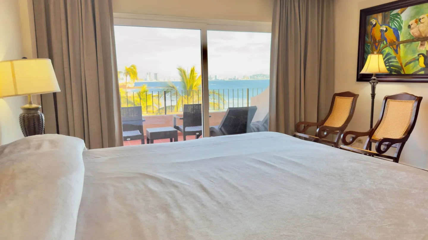 One-bed guest room with ocean-facing balcony and chairs at Hotel Playa Mazatlan.