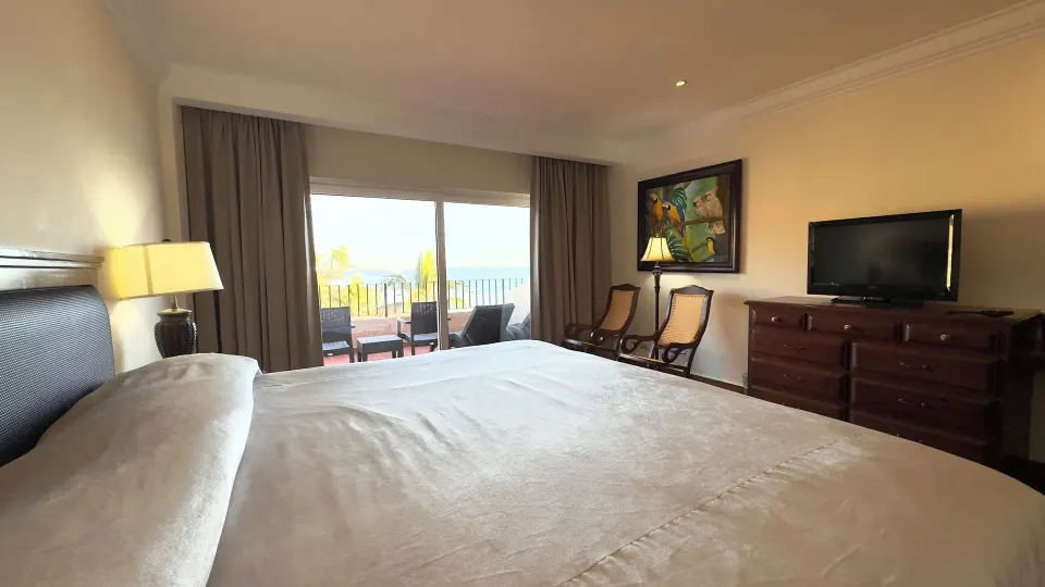 One-bed guest room with dresser, TV, balcony, and seating at Hotel Playa Mazatlan.
