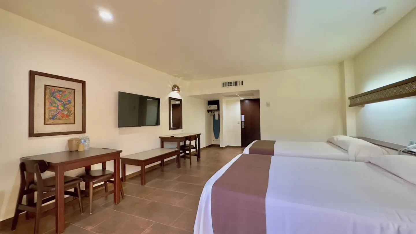 Standard room with two beds, dining table, desk, and TV at Hotel Playa Mazatlan.