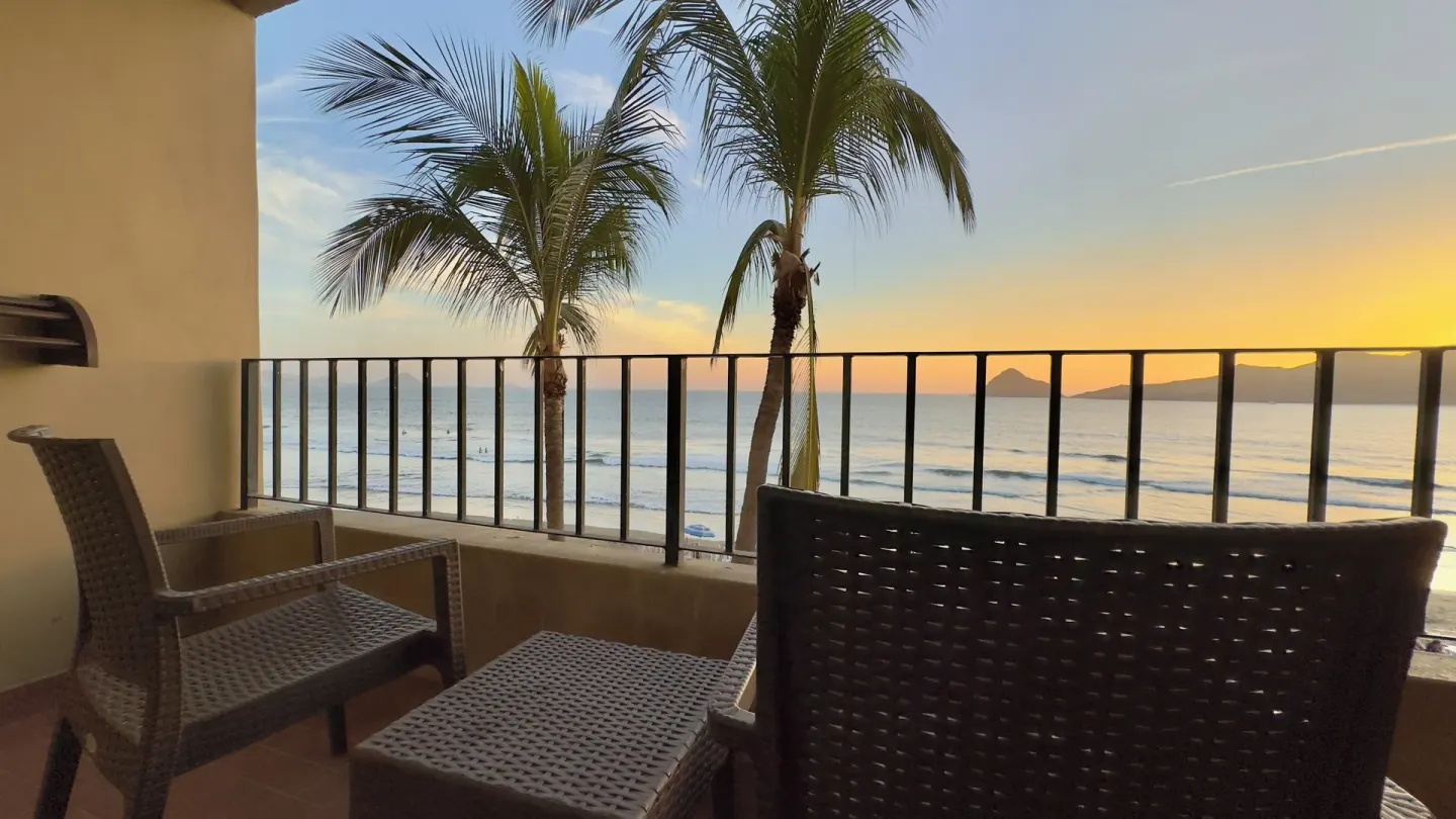 Ocean-view room balcony with wicker seating and palms at Hotel Playa Mazatlan.