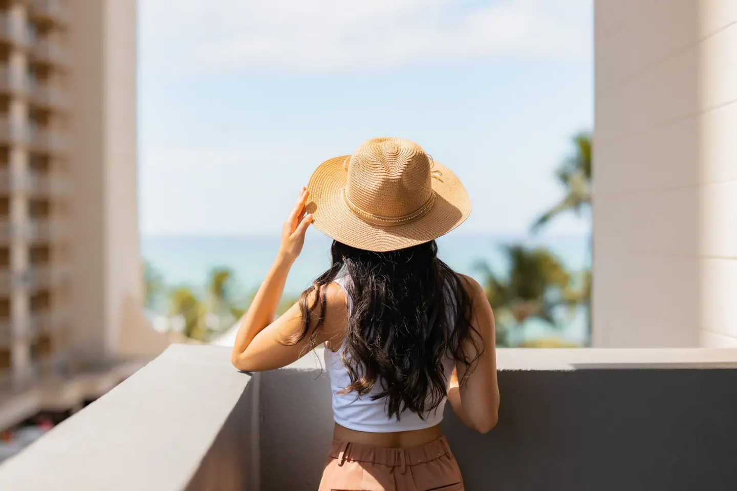 A guest in a sun hat looks toward the ocean from a balcony at Hotel Renew.