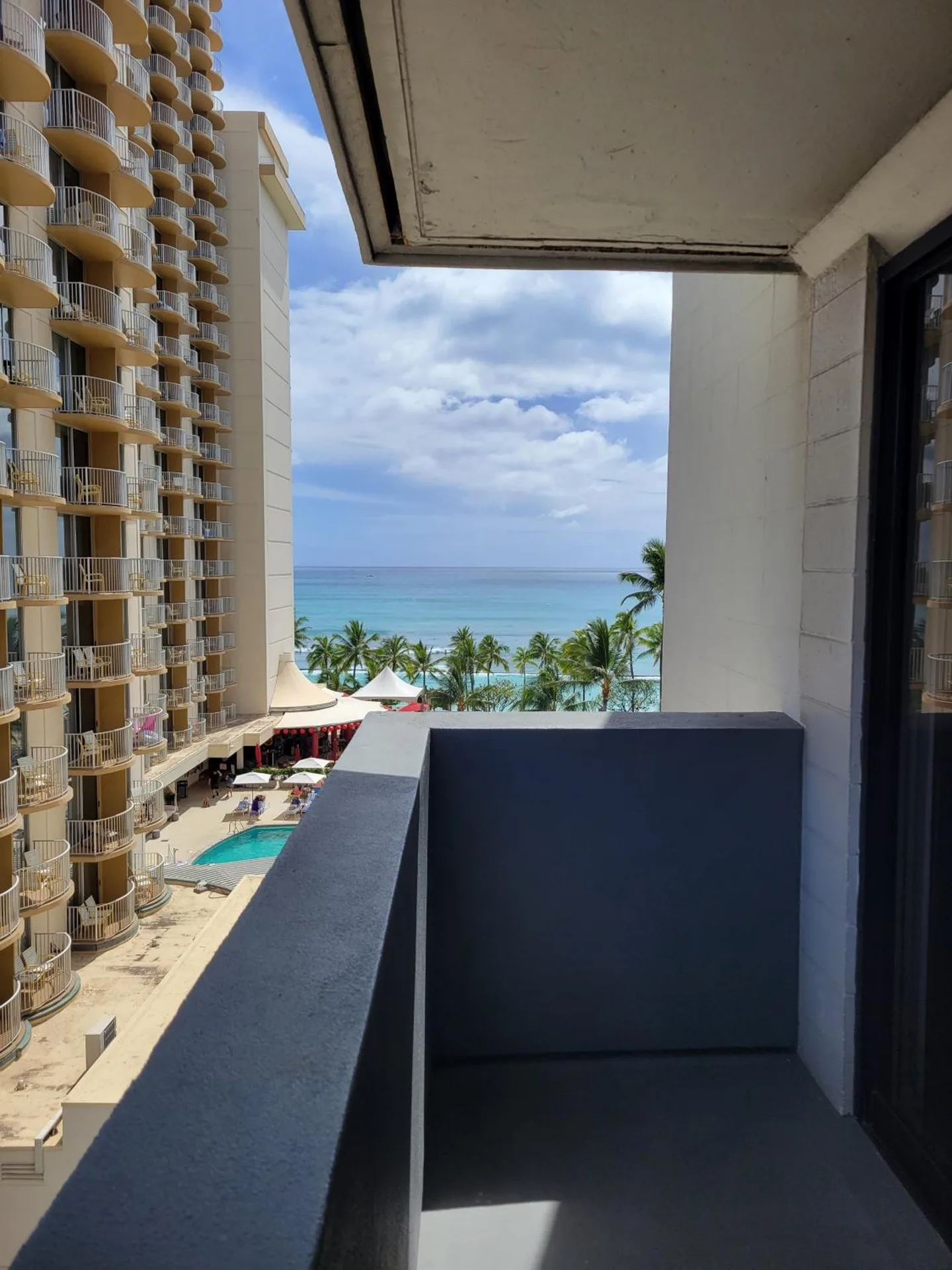 Guest balcony at Hotel Renew overlooking nearby towers, palms, pool, and ocean.