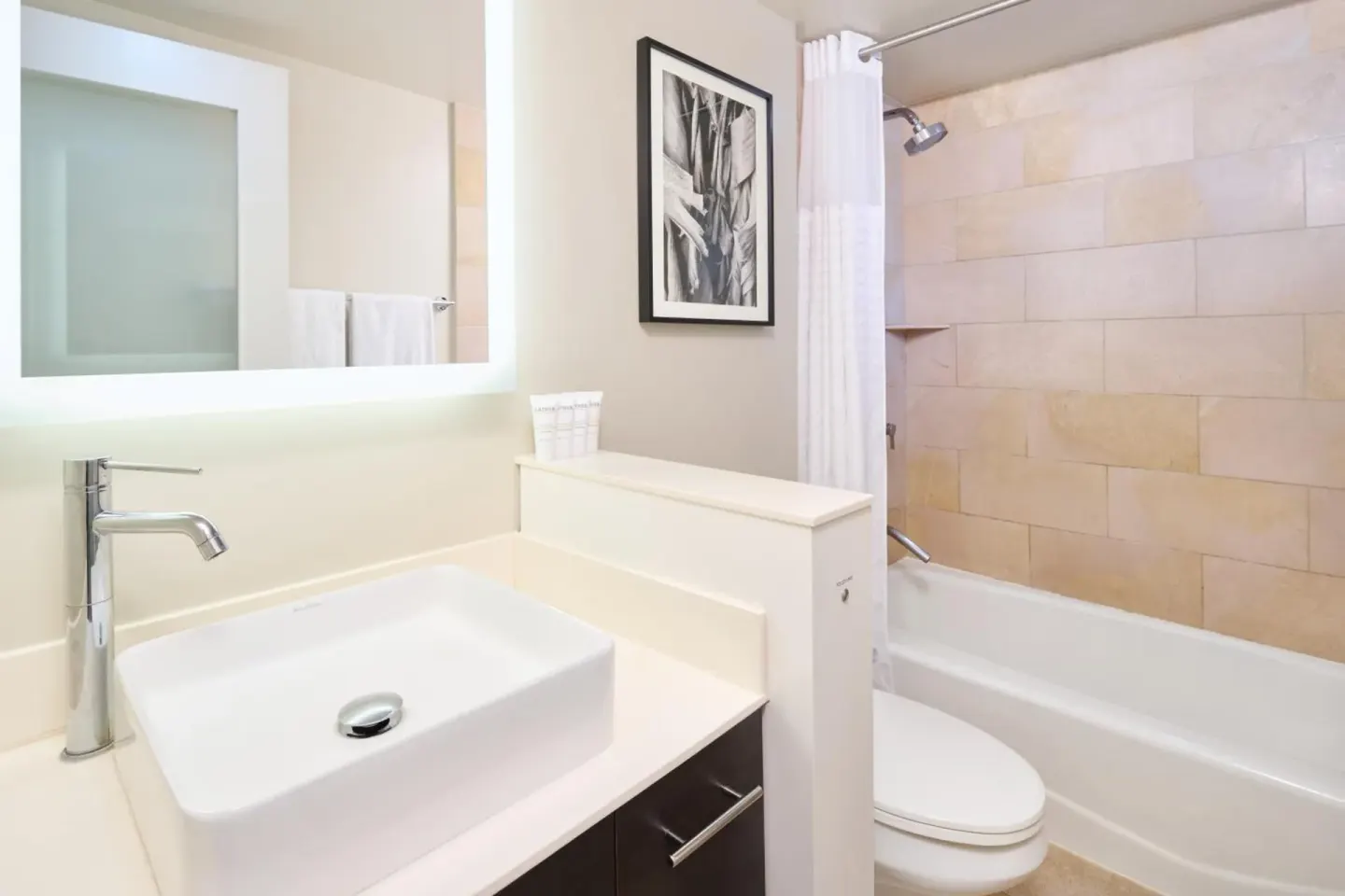 A bathroom with a vessel sink, illuminated mirror, toilet, and tub is shown at Hotel Renew.