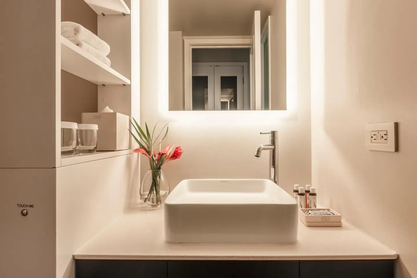 Guest room bathroom vanity at Hotel Renew with sink, mirror, towels, flowers, and bath amenities.