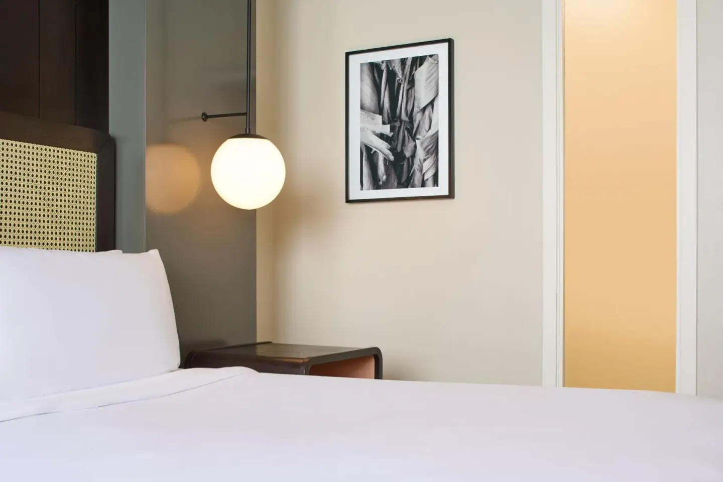 Guest room bed at Hotel Renew with white bedding, globe pendant light, and framed wall art.