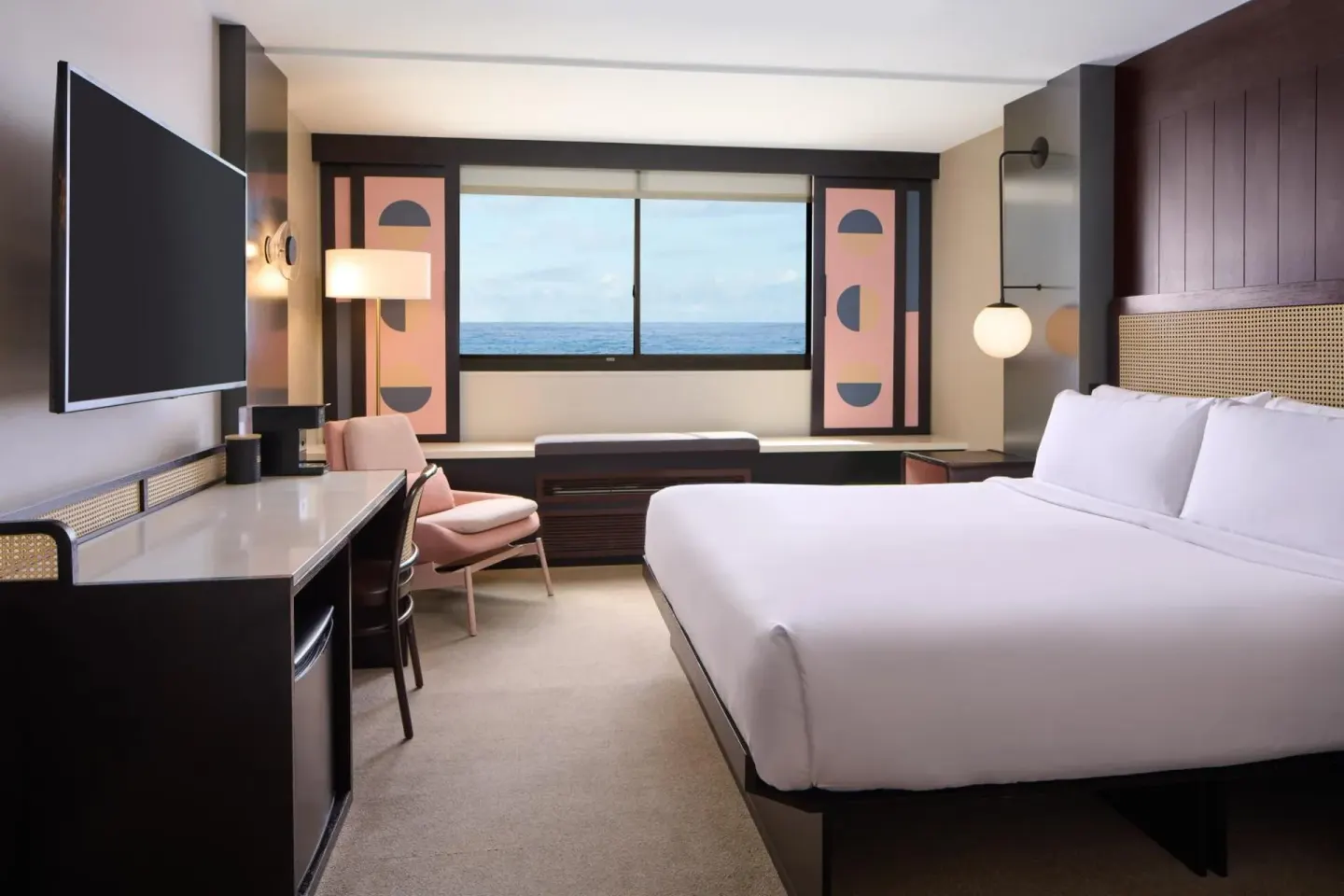 King bed guest room at Hotel Renew with desk, chair, TV, window bench, and ocean view.