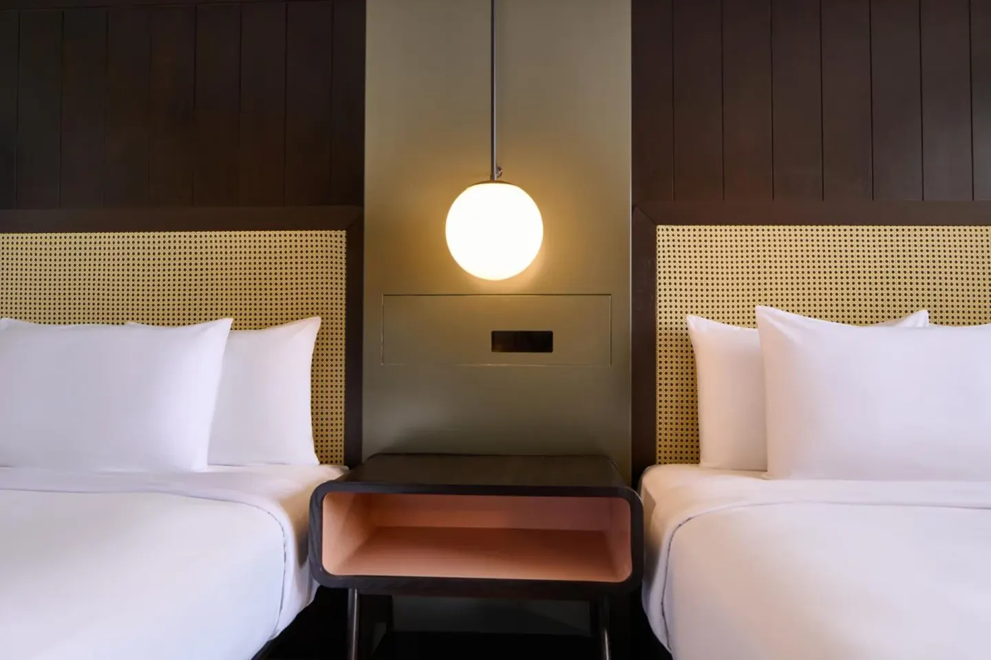 Two white beds with woven headboards and a globe light in a Hotel Renew guest room.