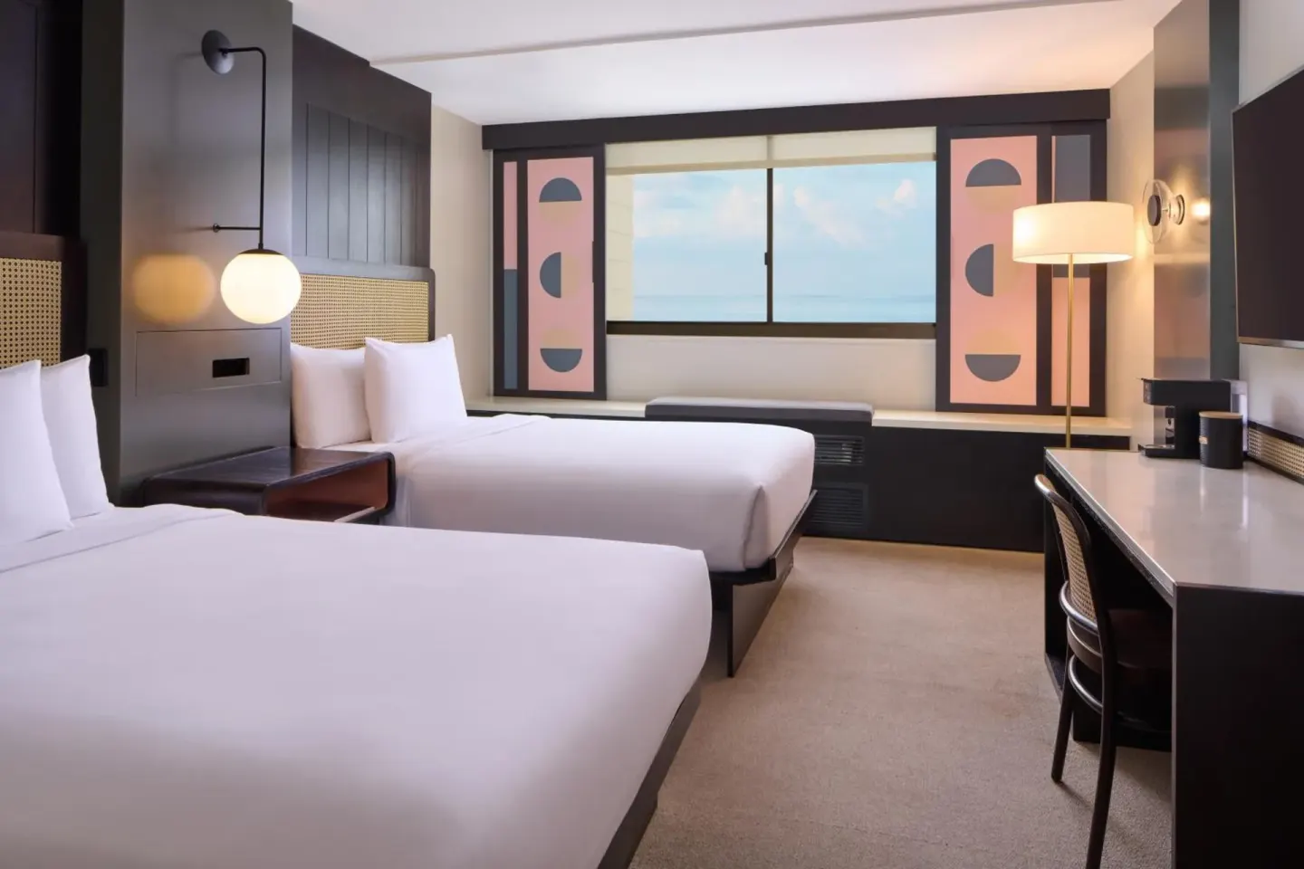 A two-bed guest room with a desk, window seat, and ocean view is shown at Hotel Renew.