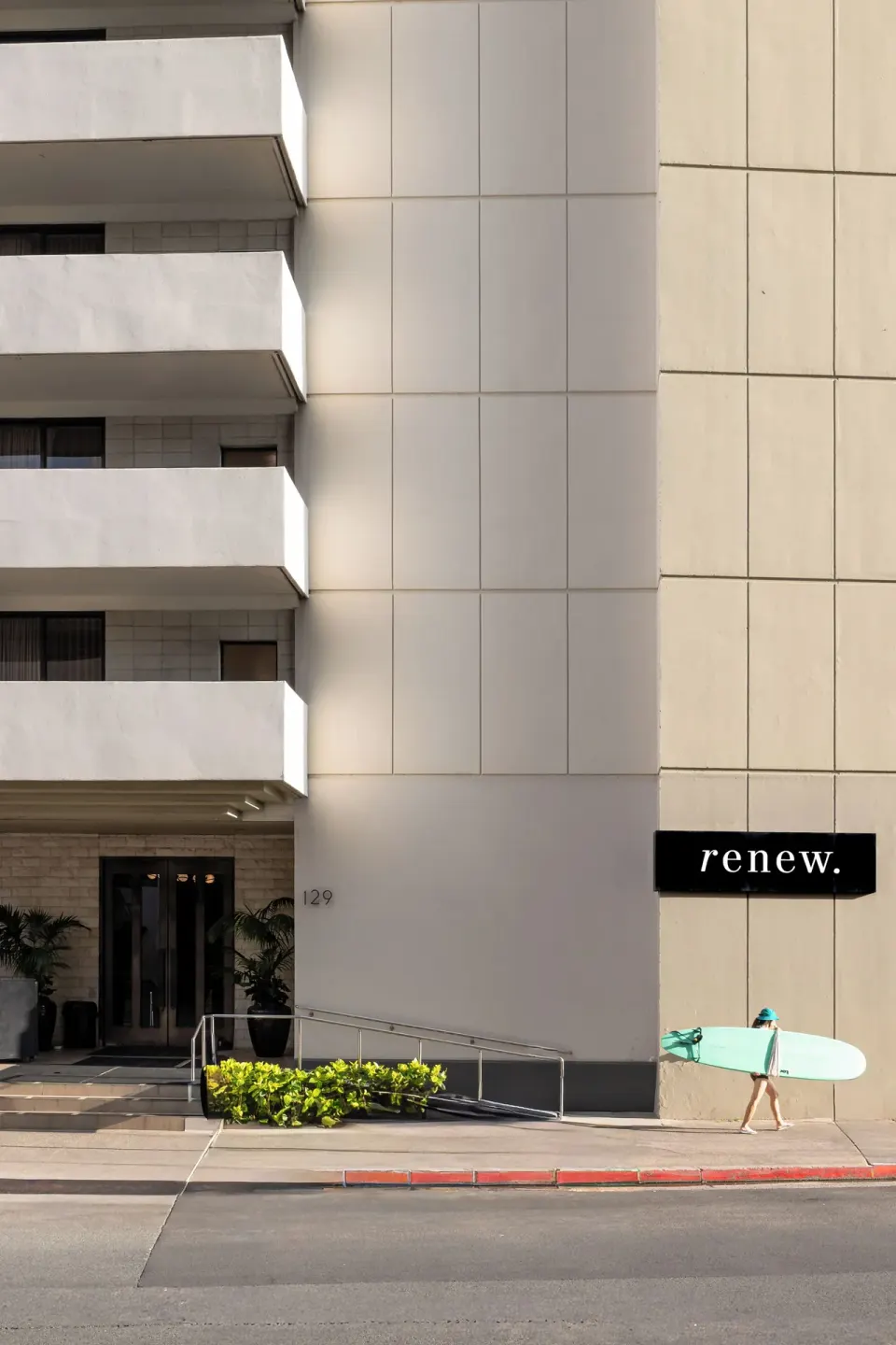 Hotel Renew street entrance and exterior sign with a pedestrian carrying a surfboard.