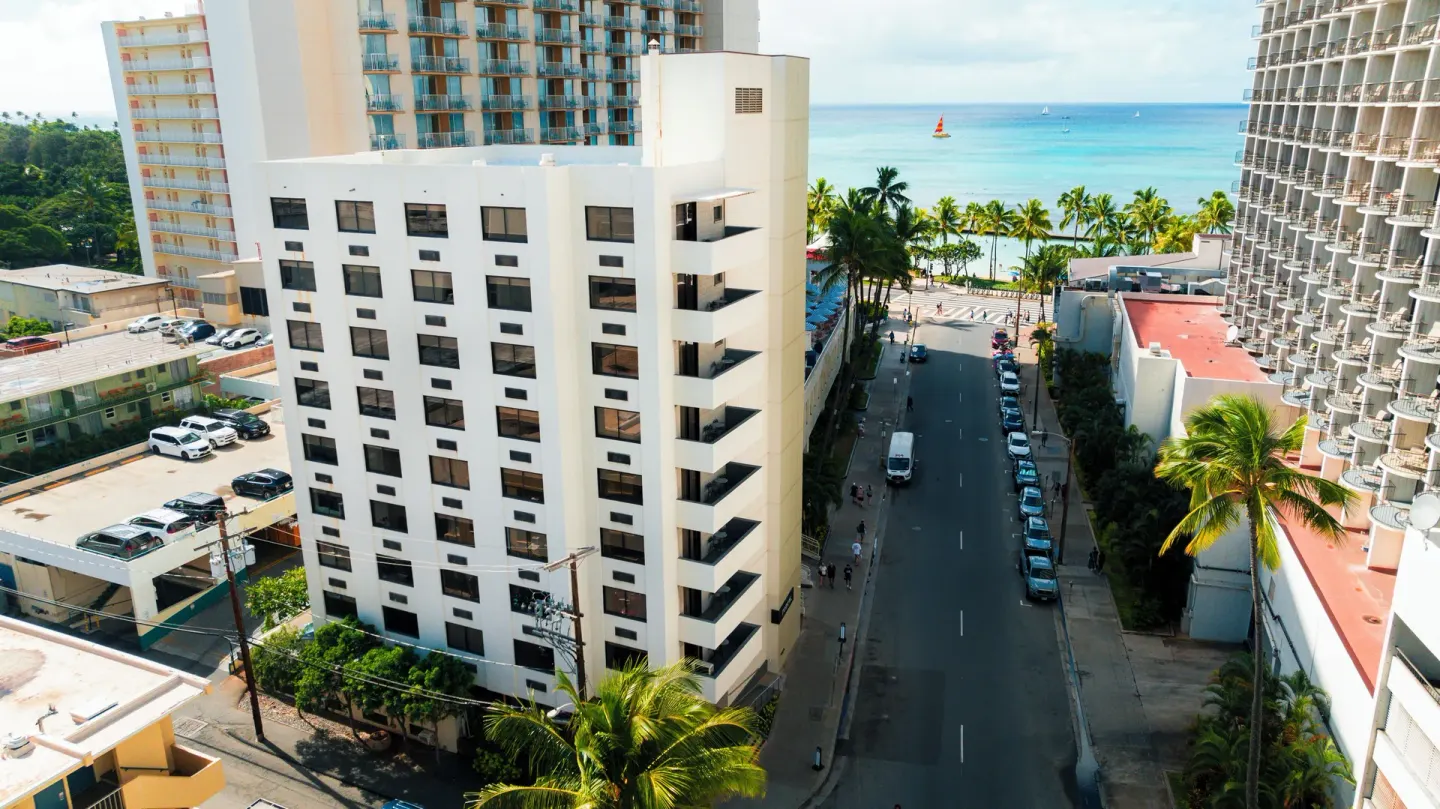 Street and ocean view from above near Hotel Renew with palms and neighboring towers.