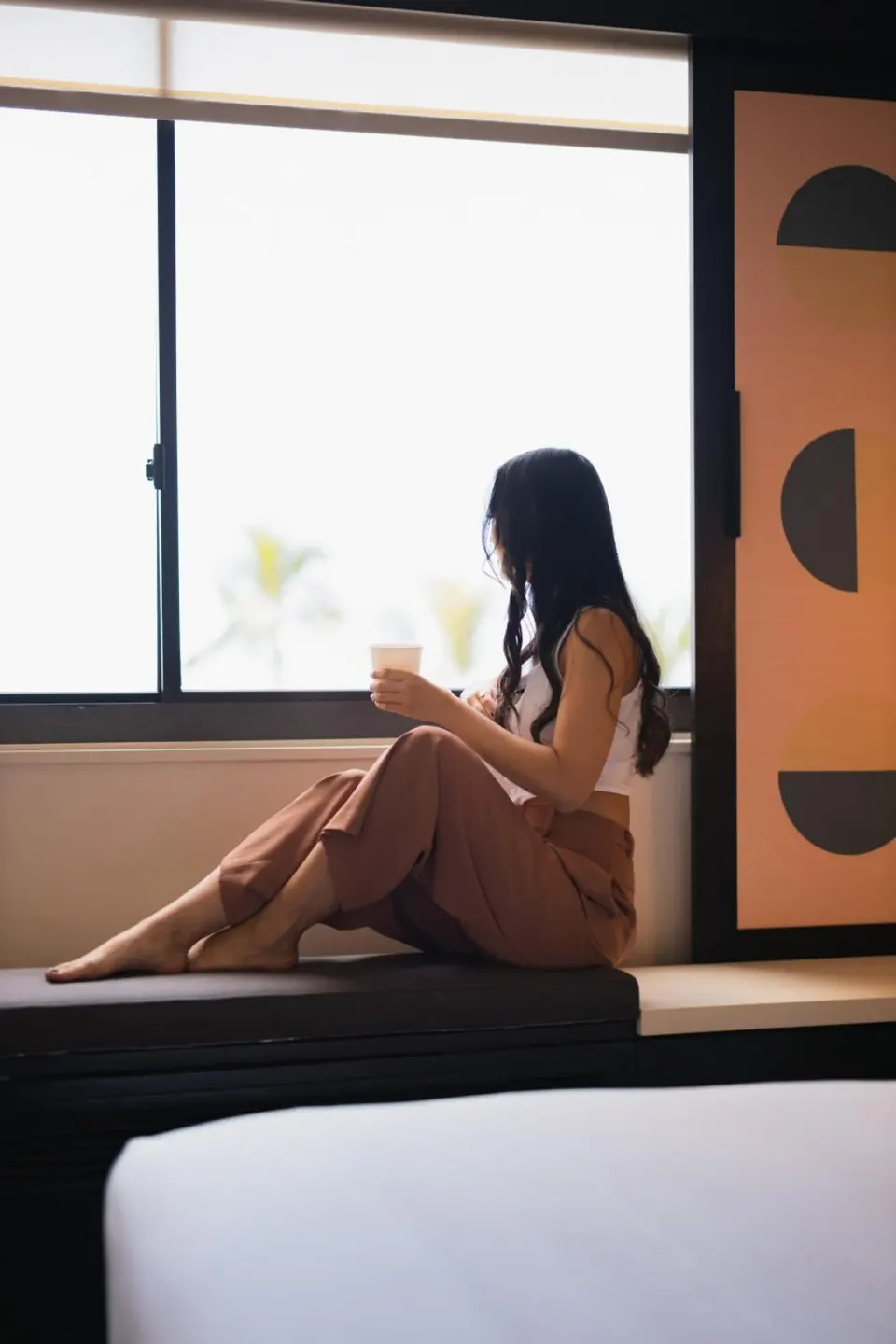 Guest sits on a window bench with a drink inside a room at Hotel Renew.