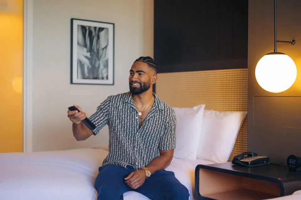A guest holding a remote on a full bed in a City View room at Hotel Renew.