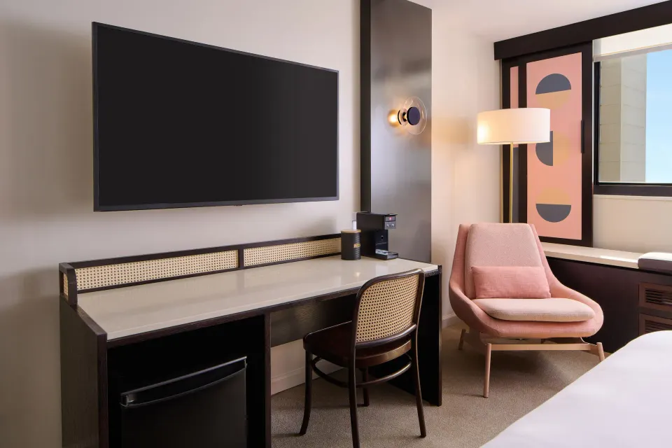 Ocean View room desk, TV, mini fridge, and pink chair beside the window at Hotel Renew.