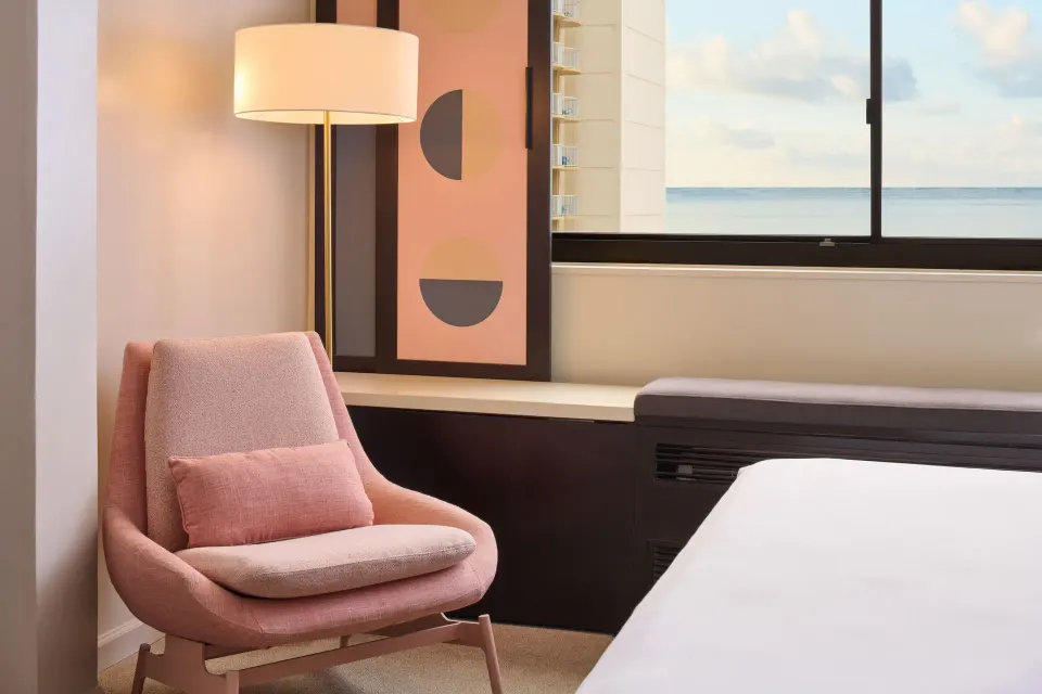 Ocean View room corner with pink lounge chair, floor lamp, bed edge, and sea view at Hotel Renew.