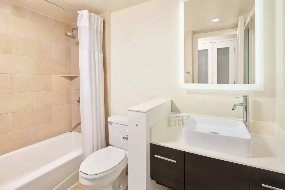 Standard Full bathroom with tub-shower, toilet, sink, and lit mirror at Hotel Renew.
