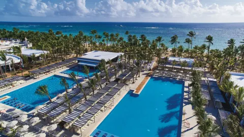 Aerial view of pools, palm trees, loungers, and beach at Hotel Riu Bambu.