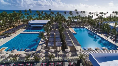 Aerial view of twin pool areas, pergola shade rows, and beachfront palms at Hotel Riu Bambu.