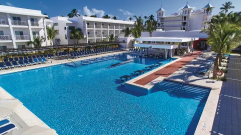 Large resort pool with bridge, swim-up bar, and surrounding loungers at Hotel Riu Bambu.