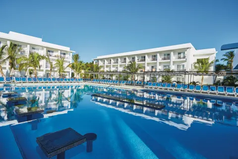 Large resort pool with blue loungers and white guest buildings at Hotel Riu Bambu.
