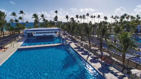 Aerial view of the pool, palms, loungers, and ocean beyond at Hotel Riu Bambu.