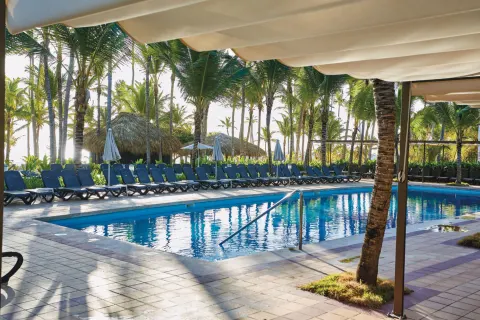 Shaded pool deck with loungers and palm trees at Hotel Riu Bambu.