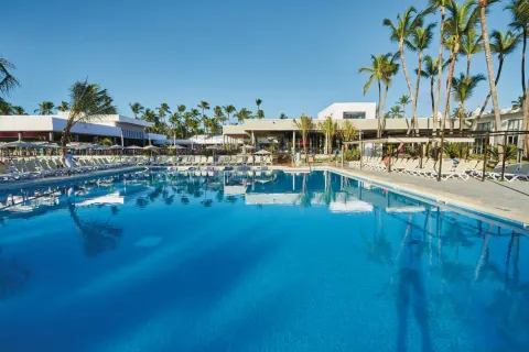 Large pool bordered by loungers, palms, and low white buildings at Hotel Riu Bambu.