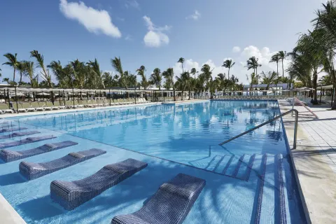 Resort pool with submerged loungers, steps, railings, and palm trees at Hotel Riu Bambu.